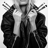 Photo en noir et blanc de l'artiste portant une veste en cuir et des pinceaux
